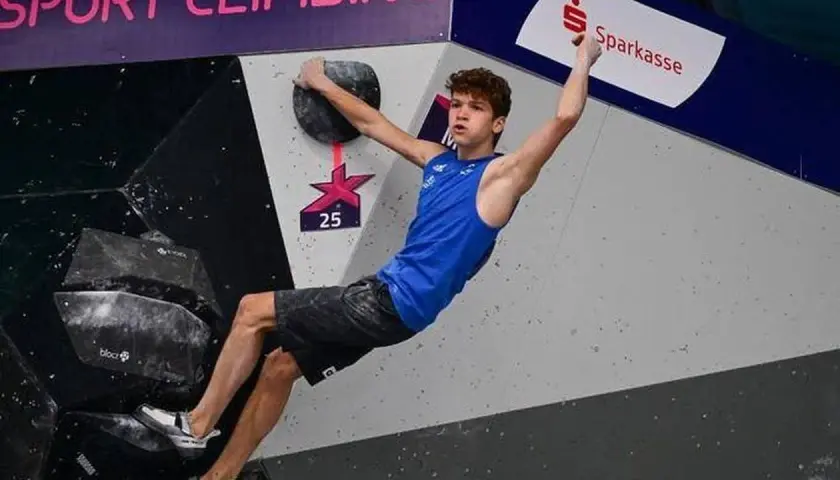 Mejdi Schalck, jeune grimpeur en action sur un mur de bloc, saisit une prise avec détermination.