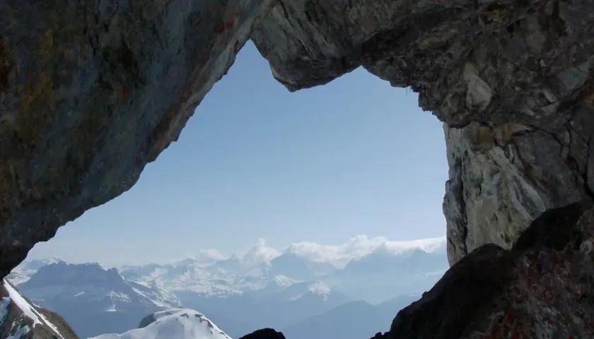 Vue spectaculaire sur les montagnes enneigées depuis le "Trou de la Mouche", un passage rocheux offrant une perspective unique lors d'une randonnée.