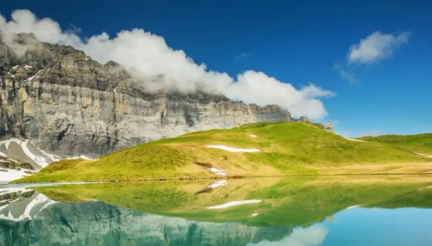 Reflets parfaits d'une montagne imposante et d'une colline verdoyante dans un lac alpin paisible, évoquant la sérénité du tour des Fiz.
