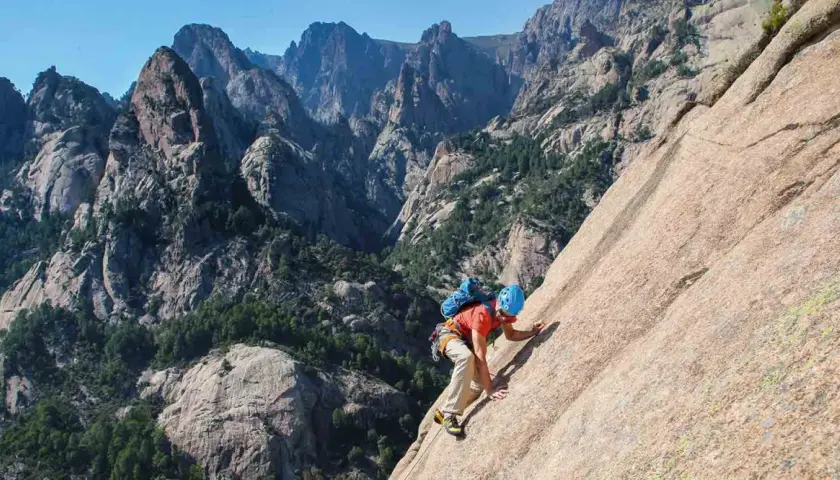 Un grimpeur en plein effort sur un rocher, avec les majestueuses montagnes de Bavella en arrière-plan. L'escalade bavella offre des vues spectaculaires.