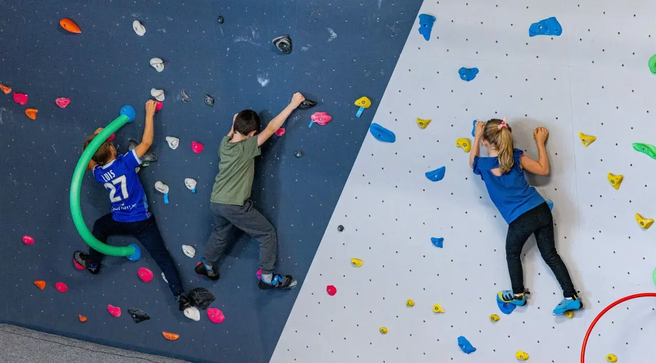 Trois enfants s'amusent lors d'une bloc session à Vienne, grimpant sur un mur coloré avec des prises variées.