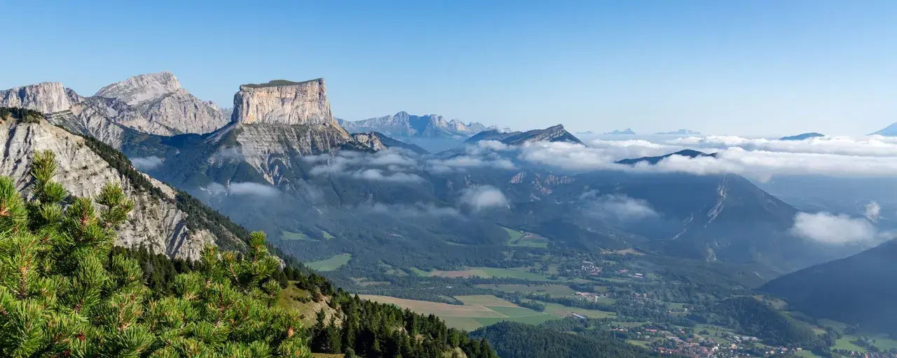 Vue panoramique du Vercors en été. Des montagnes majestueuses, des nuages bas et une forêt verdoyante invitent à explorer ce paysage magnifique.