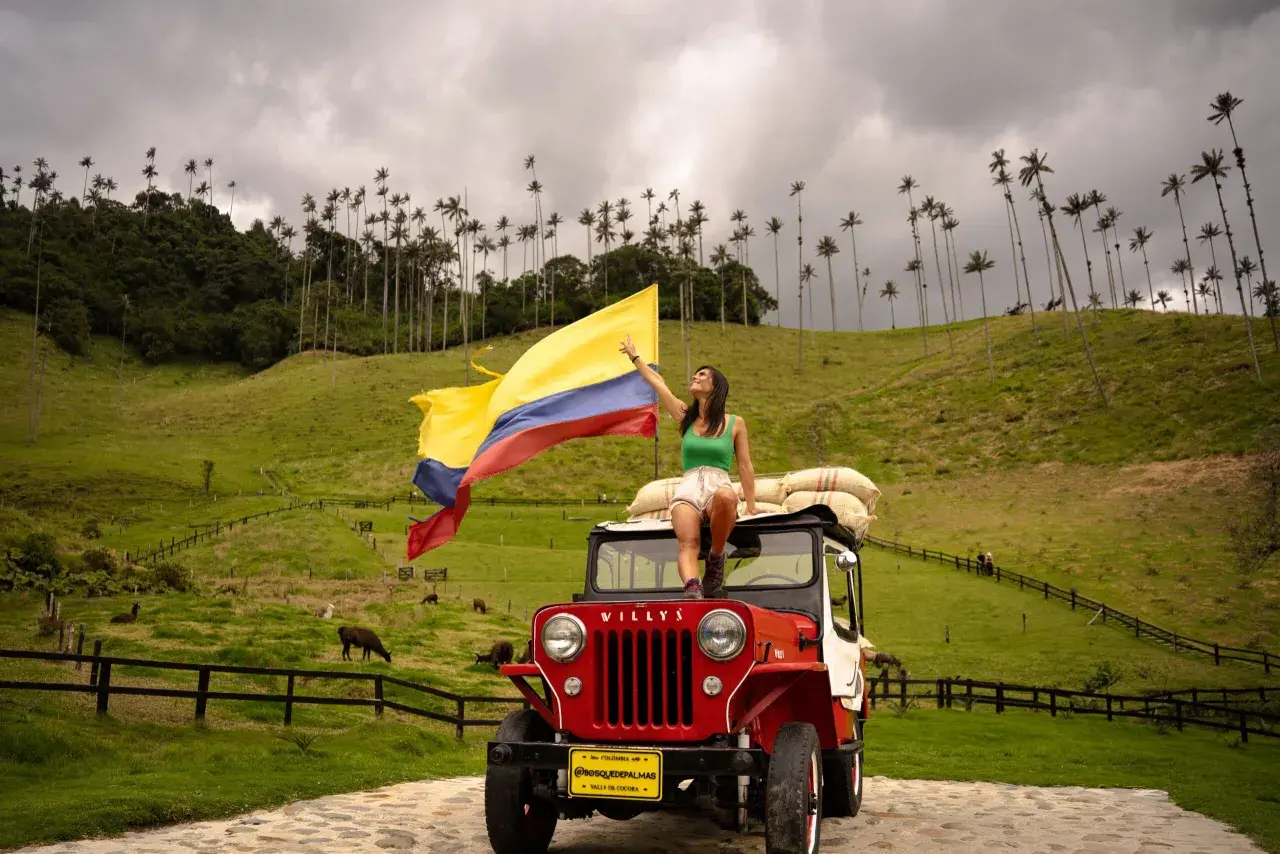 Femme sur une jeep rouge, drapeau colombien flottant, au milieu des palmiers de cire de la Vallée de Cocora, Colombie.