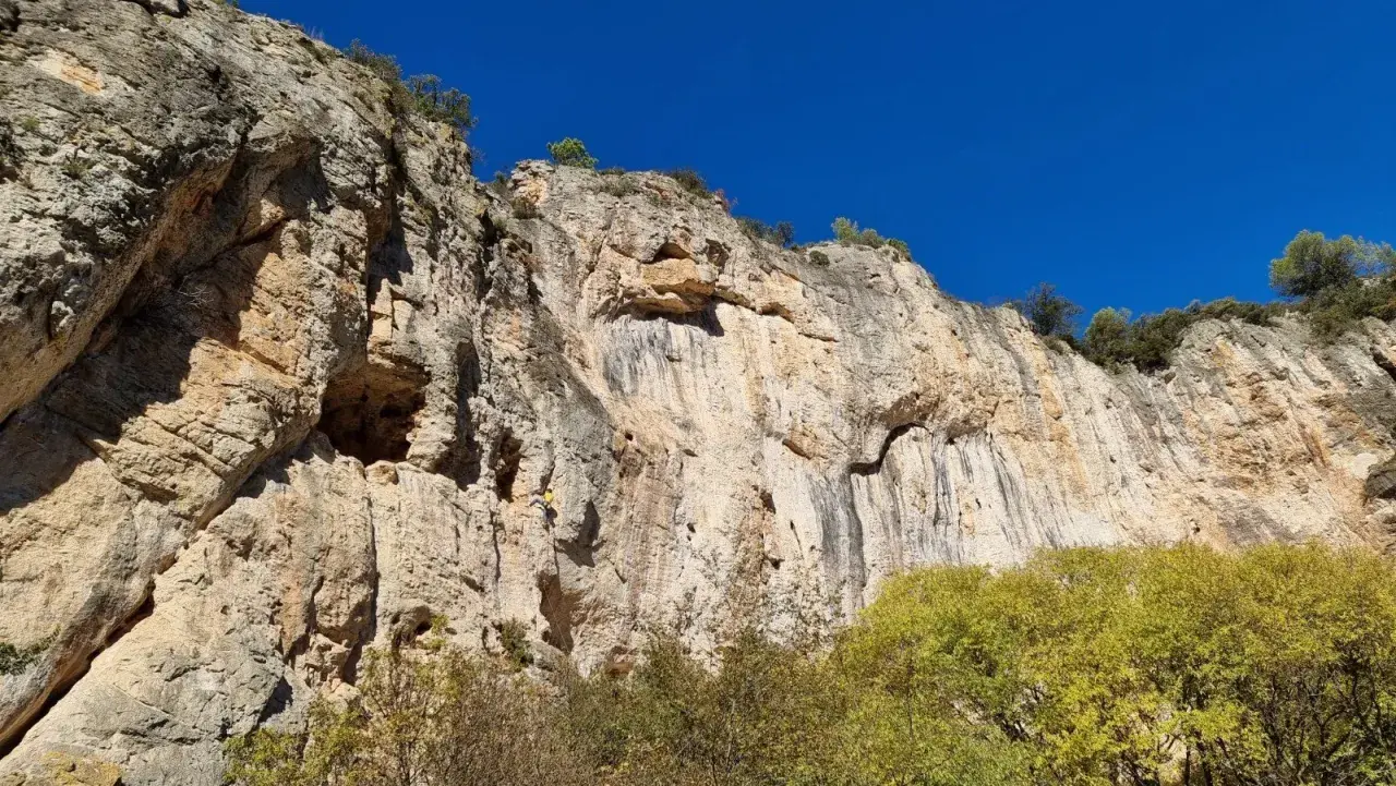 Un grimpeur jaune défie la falaise imposante, un véritable chateauvert pour l'escalade. Le ciel bleu azur surplombe ce paysage rocheux.