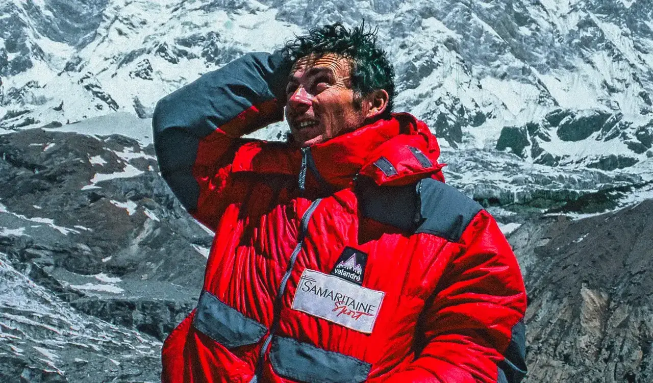 Jean-Christophe Lafaille, le visage marqué par l'effort, se protège du soleil sur fond de montagnes enneigées.