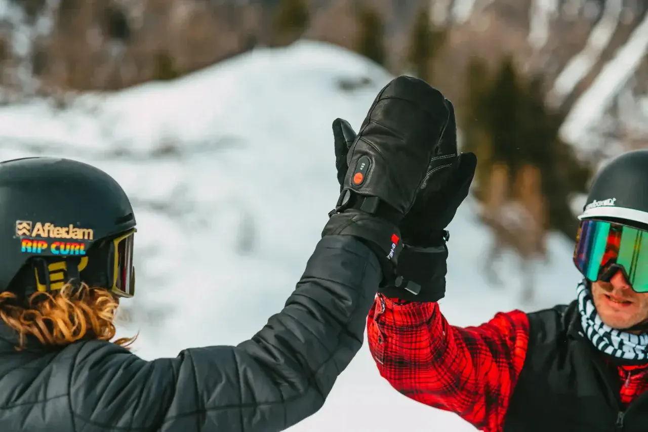 Deux skieurs se donnent une tape dans la main, portant des casques et des lunettes de ski. L'un d'eux a des gants noirs chauffants, une marque de ski de qualité.