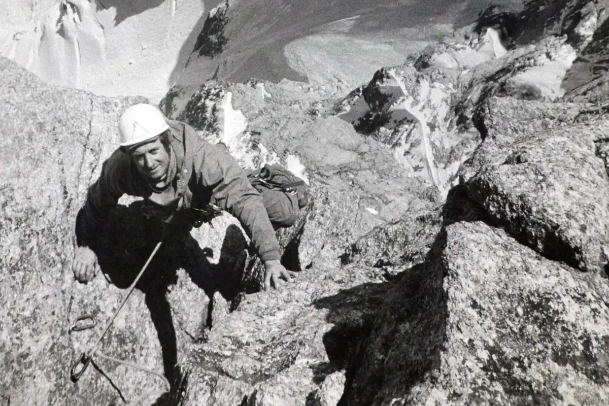 Serge Gousseault, alpiniste chevronné, escalade une paroi rocheuse escarpée, casque blanc sur la tête.