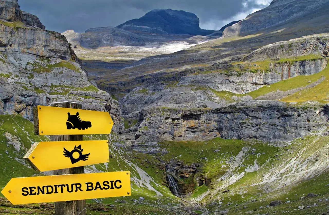 Panneau jaune indiquant "SENDITUR BASIC" dans une vallée montagneuse spectaculaire.