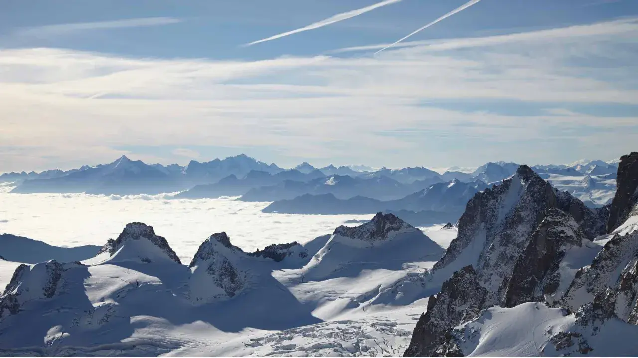 Vue panoramique d'une majestueuse montagne France enneigée, avec des sommets bleutés à l'horizon et une mer de nuages blancs.