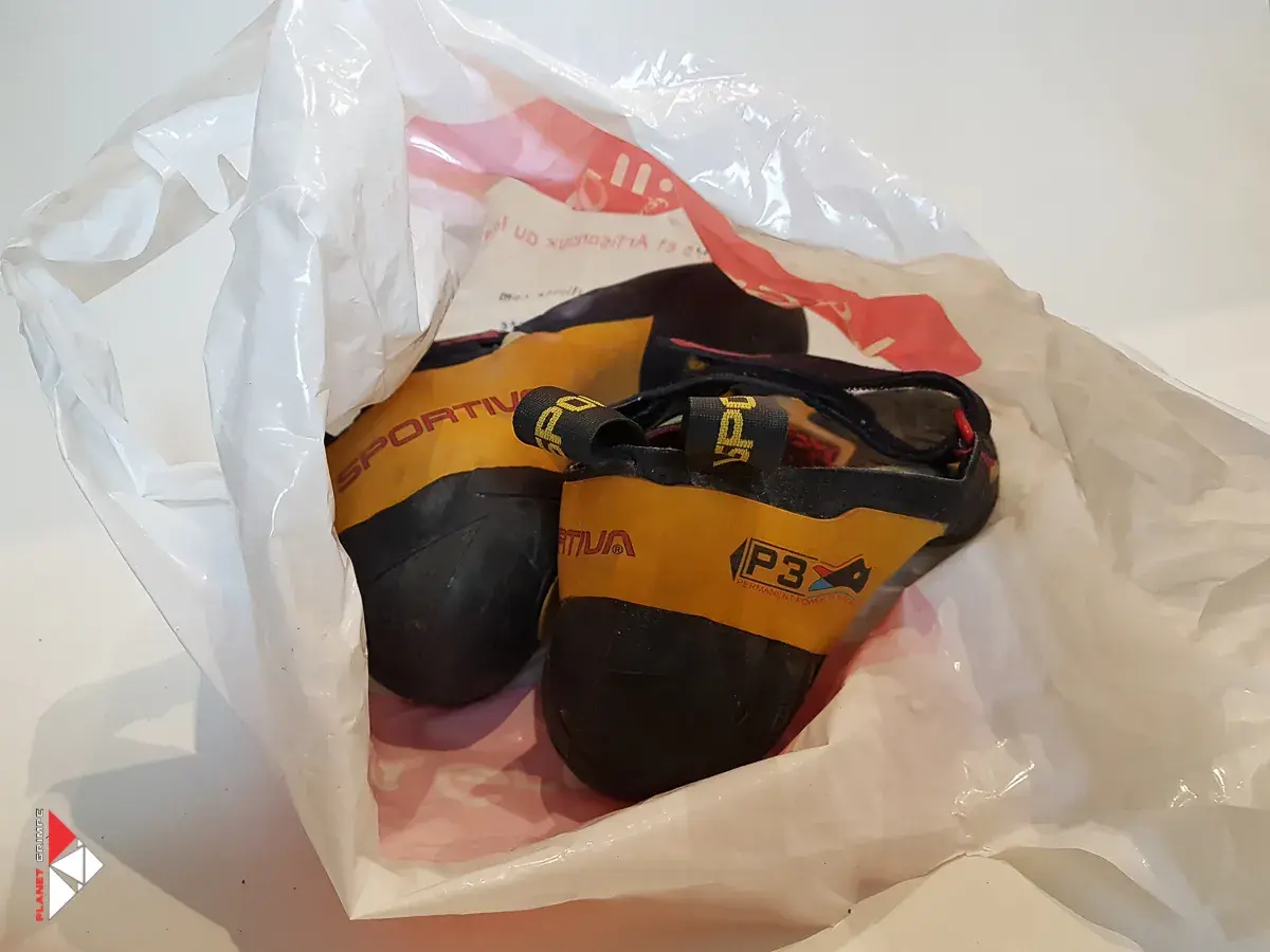Une paire de chaussons d'escalade Sportiva jaunes et noirs, visiblement un chausson qui pue, dans un sac en plastique blanc.