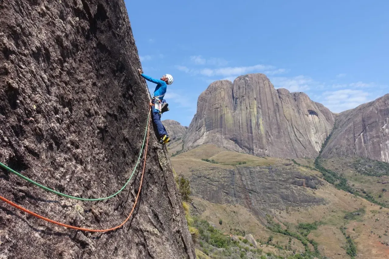 Un grimpeur en pleine ascension sur un rocher impressionnant, avec des montagnes majestueuses en arrière-plan. Une aventure d'escalade à Madagascar.