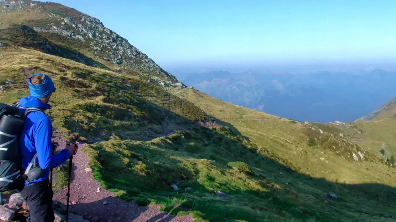 Un randonneur en bleu, prêt pour son premier trek, admire le paysage montagneux.