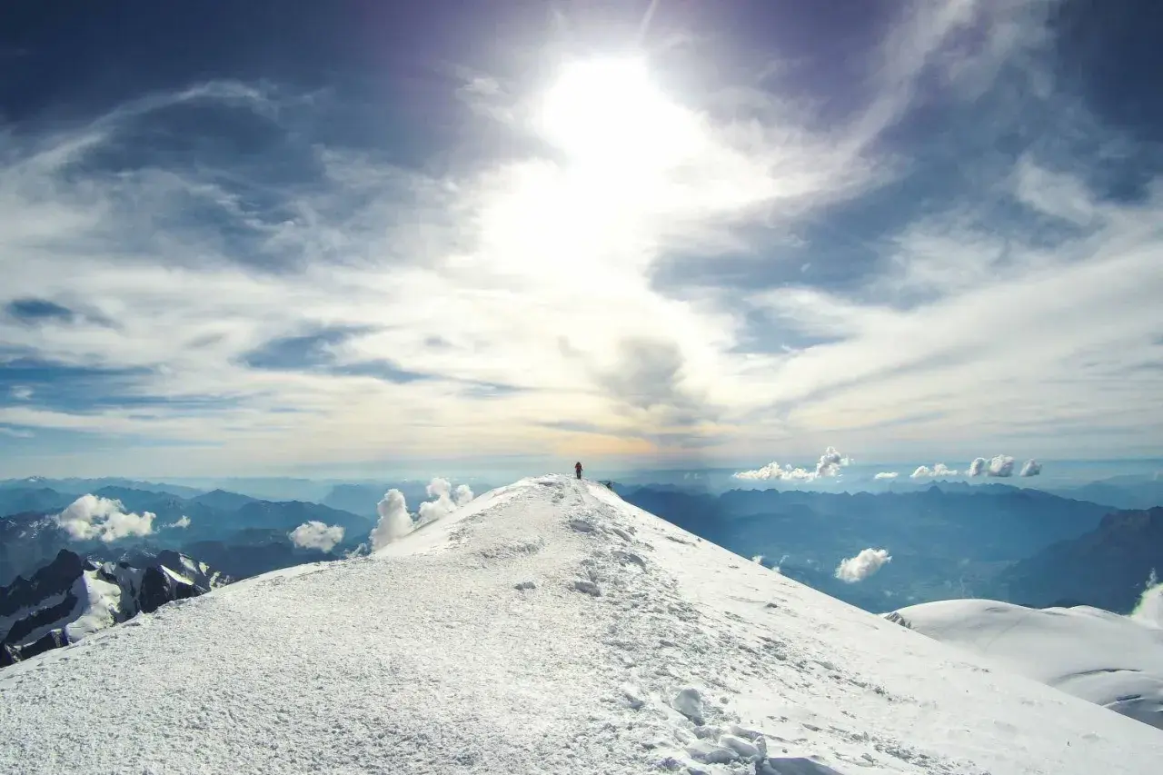 Un alpiniste solitaire au sommet du Mont Blanc, sous un ciel spectaculaire.