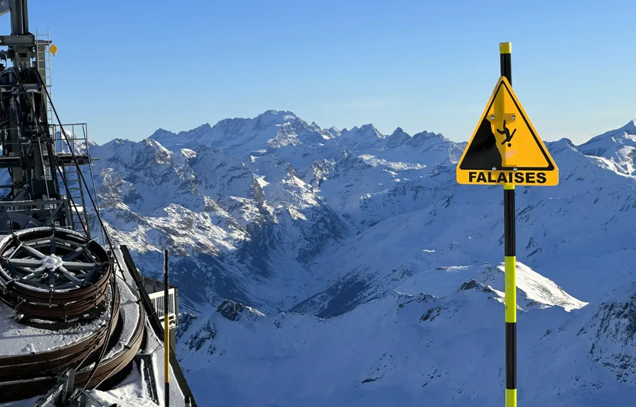 Panneau "Falaises" sur fond de montagnes enneigées, avec une remontée mécanique. Attention aux neiges mouvantes et aux dangers du relief.