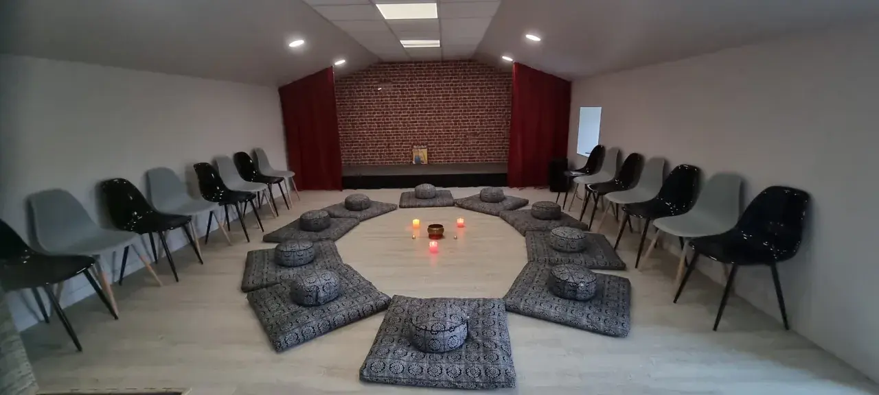 Salle de méditation avec coussins disposés en cercle et bougies allumées. Des chaises attendent autour, créant une atmosphère paisible, comme un refuge au petit goulet.