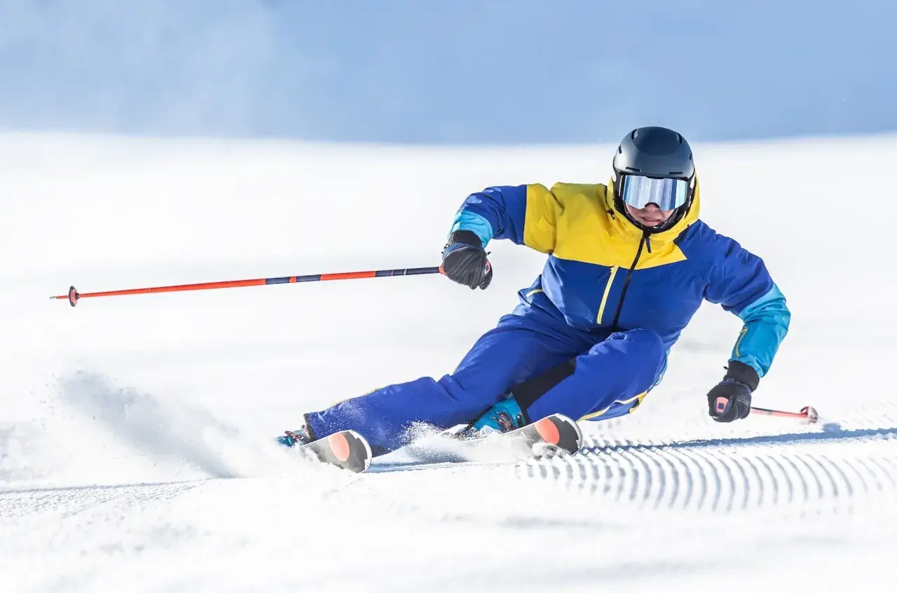 Un skieur en combinaison jaune et bleue vire sur la neige, ses skis paraboliques taillant la piste.