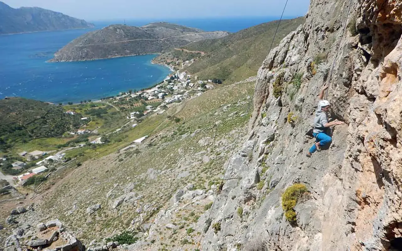 Grimpeur en action sur les falaises de Kalymnos, avec une vue imprenable sur la mer Égée et le village en contrebas.