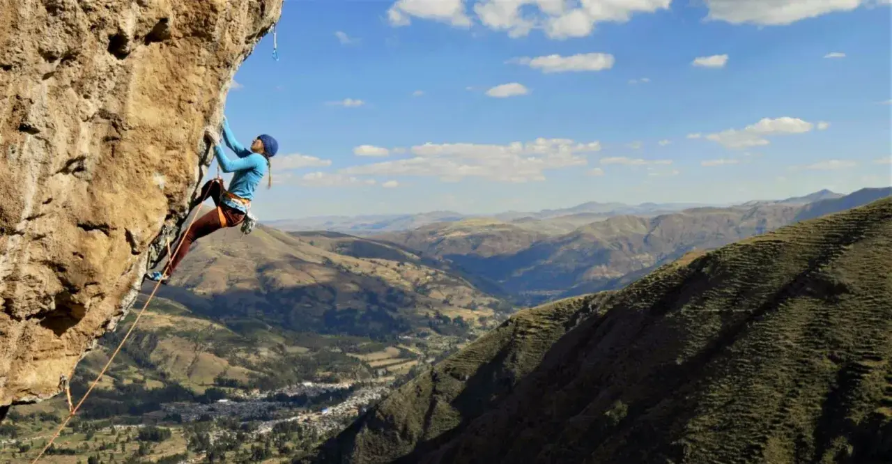 Charlotte Durif, grimpeuse audacieuse, défie la falaise rocheuse sous un ciel bleu. Paysage montagneux spectaculaire en arrière-plan.