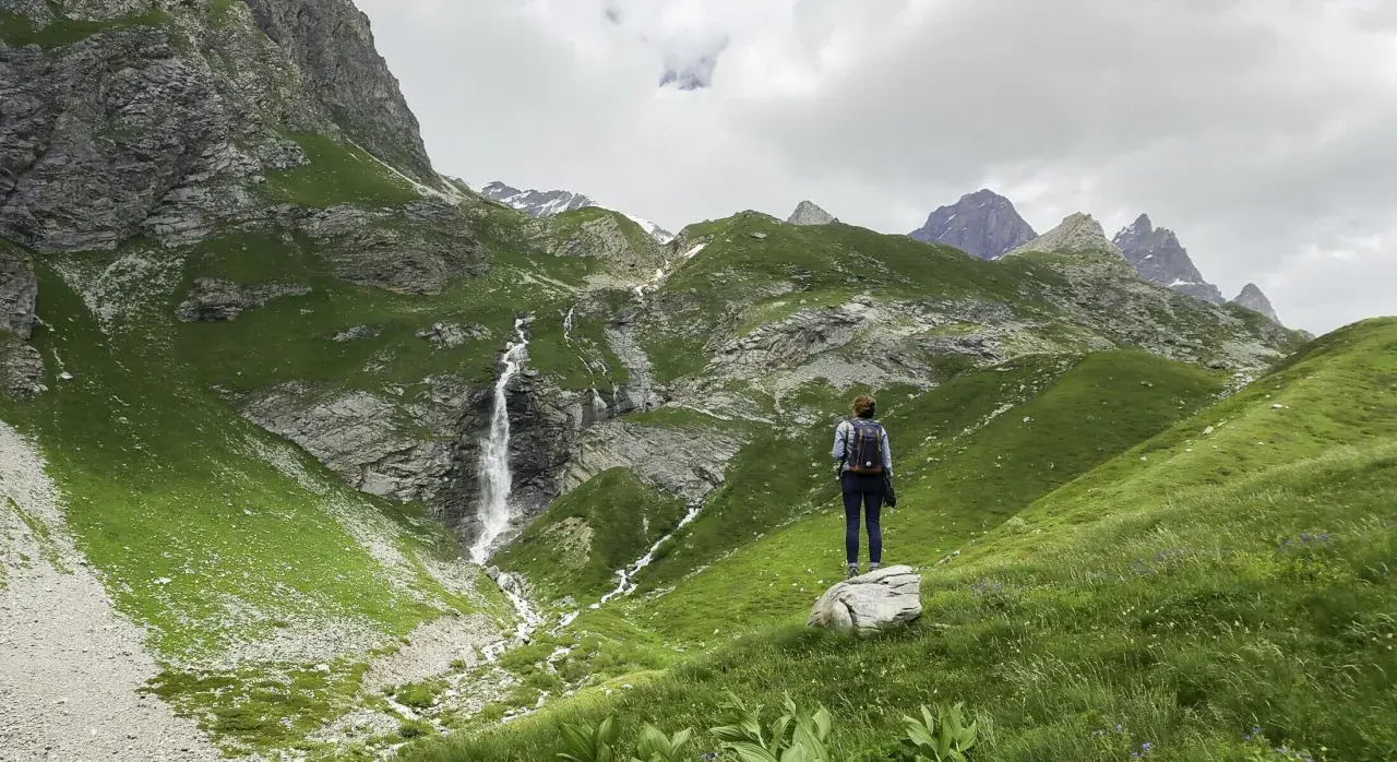 Une randonnée dans les Bauges, avec une cascade impressionnante et des montagnes verdoyantes. Une femme admire le paysage.