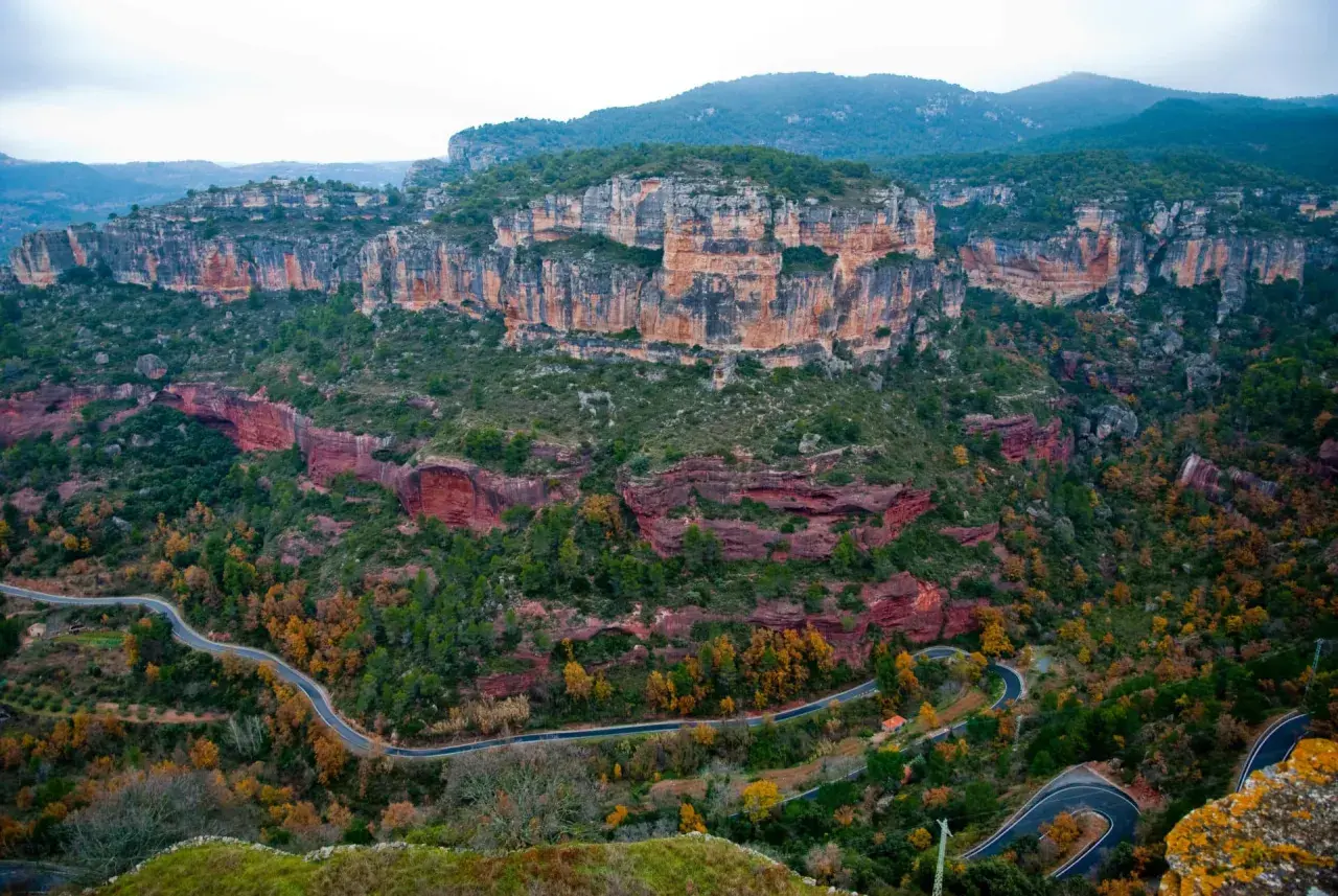 Paysage spectaculaire de falaises rouges et vertes, avec une route sinueuse traversant la vallée. Un paradis pour la siurana escalade.