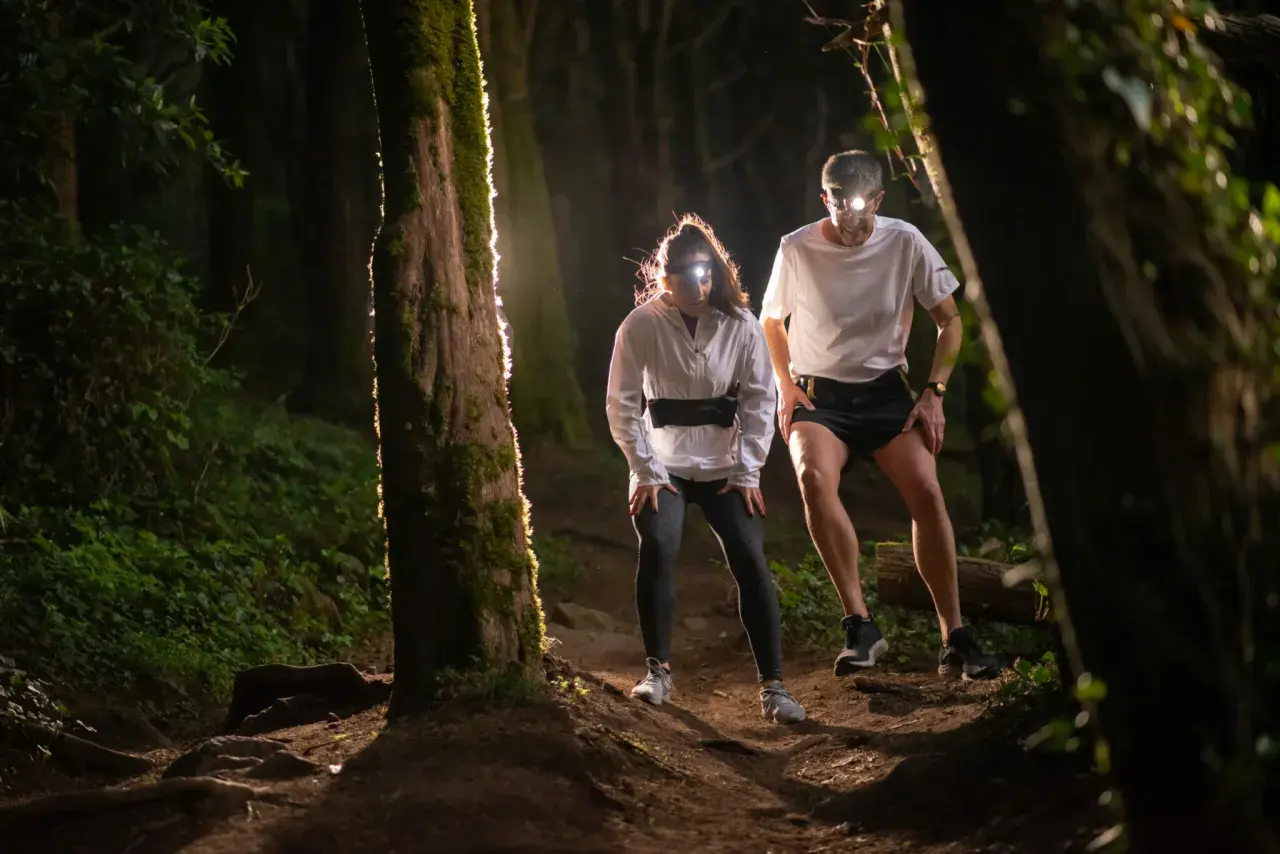 Deux coureurs équipés de lampes frontales s'aventurent sur un sentier forestier sombre. Une **randonnée nocturne** pleine d'adrénaline.