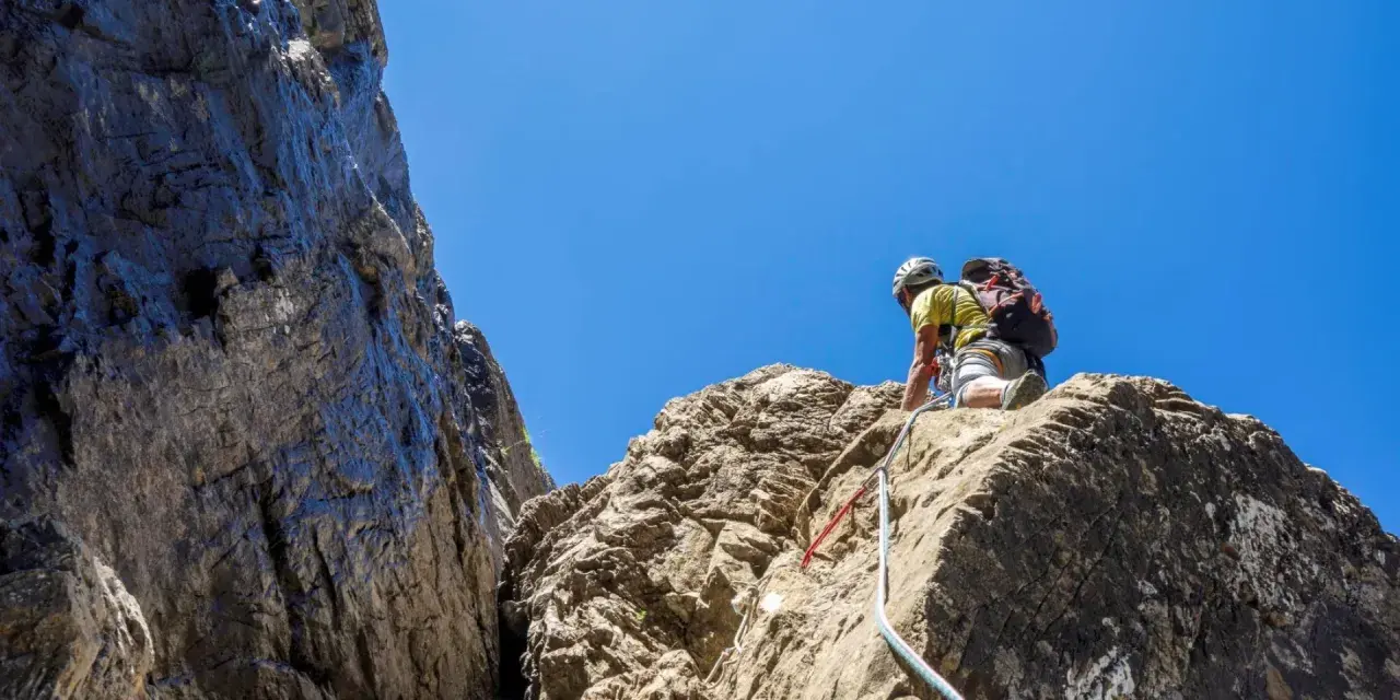 Un grimpeur en plein effort, casque et sac à dos, s'engage sur une paroi rocheuse. L'escalade dans les Pyrénées offre des vues spectaculaires.