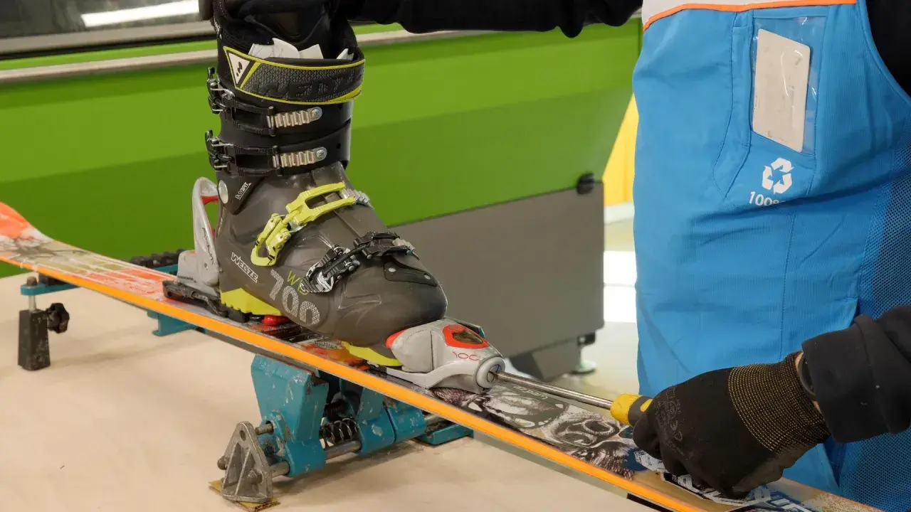 Réglage d'une fixation de ski sur un tableau de fixation. Un skieur ajuste la fixation avec un tournevis.