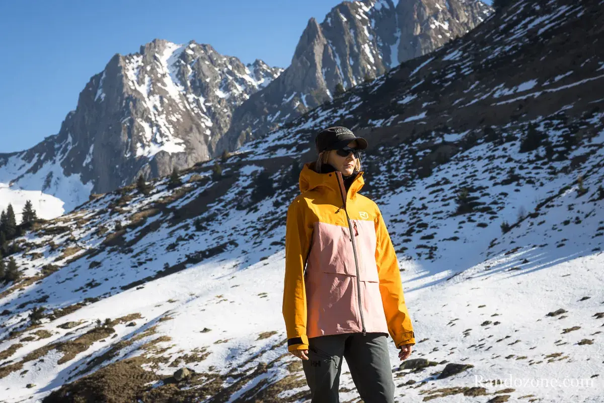 Une femme porte une veste shell colorée, idéale pour affronter les montagnes enneigées.