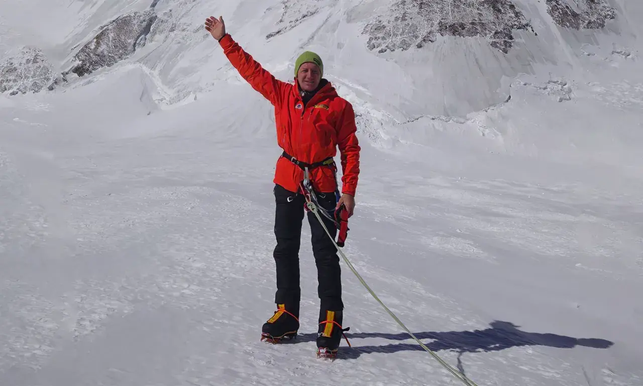 Denis Urubko, alpiniste chevronné, salue depuis un sommet enneigé, prêt pour l'ascension.