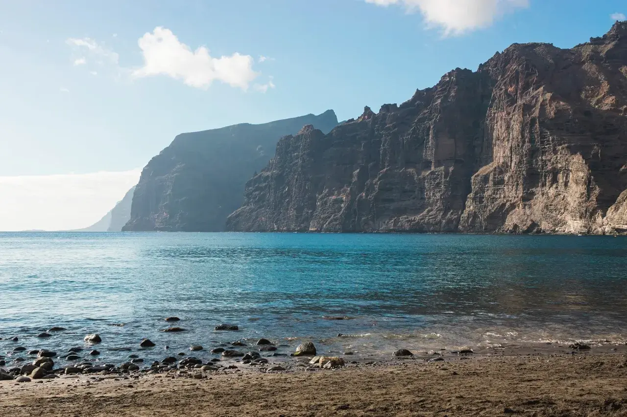 Les falaises de Los Gigantes se dressent majestueusement au-dessus de l'océan bleu. Le rivage est couvert de sable et de galets.