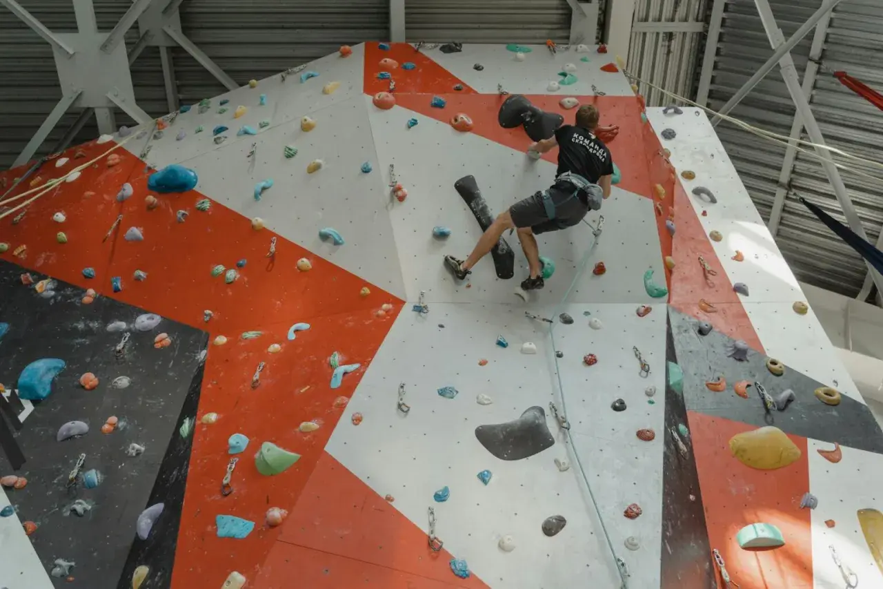 Un grimpeur s'entraîne pour **climb up** sur un mur d'escalade intérieur aux couleurs vives, utilisant des prises variées.