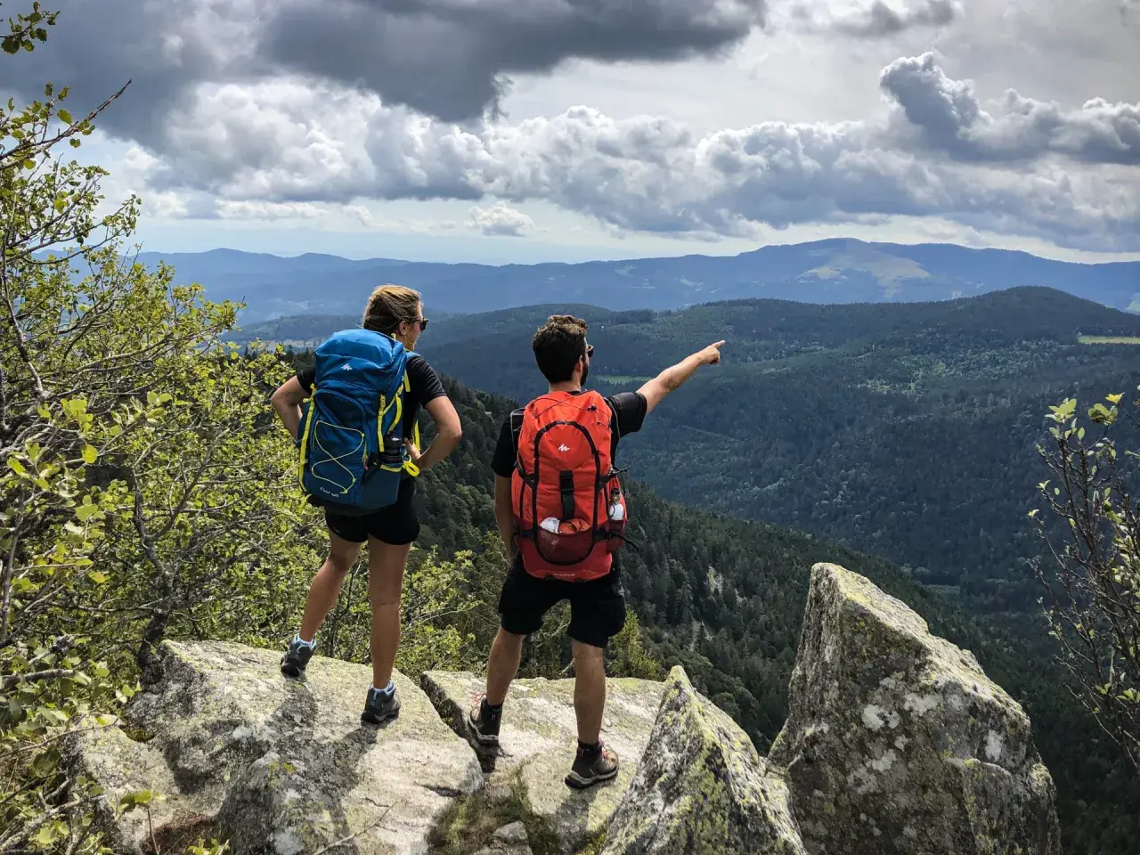 Deux randonneurs contemplent un paysage de montagnes et de forêts. Une balade Vosges facile pour admirer la vue.