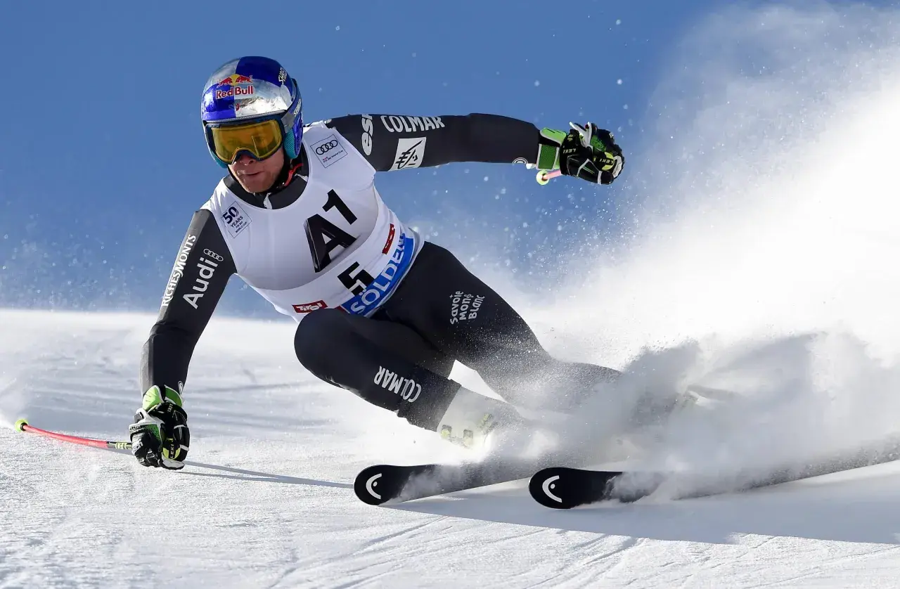 Un skieur acrobatique en plein virage, projetant de la neige avec ses skis rocker. Casque Red Bull, combinaison Colmar.