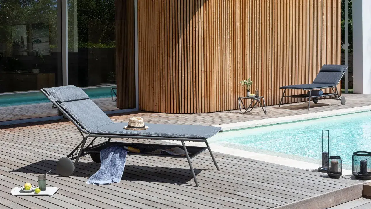 Chaises longues Lafuma près d'une piscine, avec une serviette bleue et un chapeau de paille. Ambiance détente estivale.