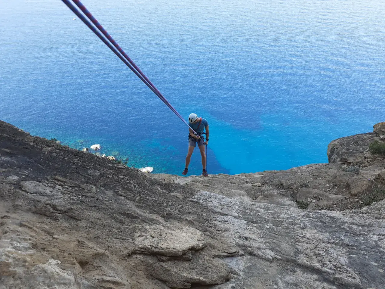 Un grimpeur se prépare pour une descente en rappel au Cap Canaille, avec la mer d'un bleu intense en contrebas. L'escalade offre une vue spectaculaire.