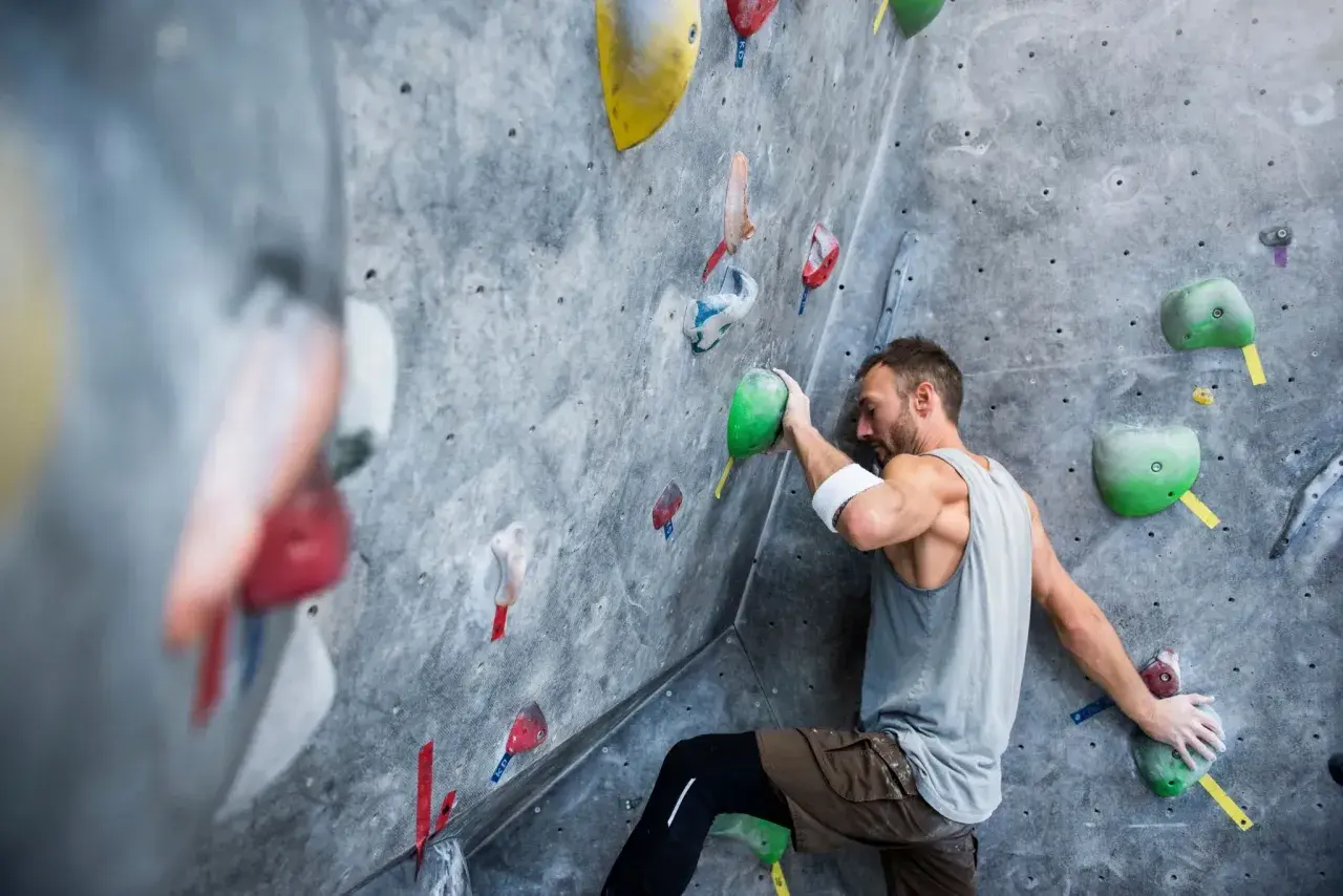 Un grimpeur concentré sur un mur d'escalade, cherchant la prise parfaite. Une scène d'escalade qui pourrait bien finir en humour si la prise glisse !