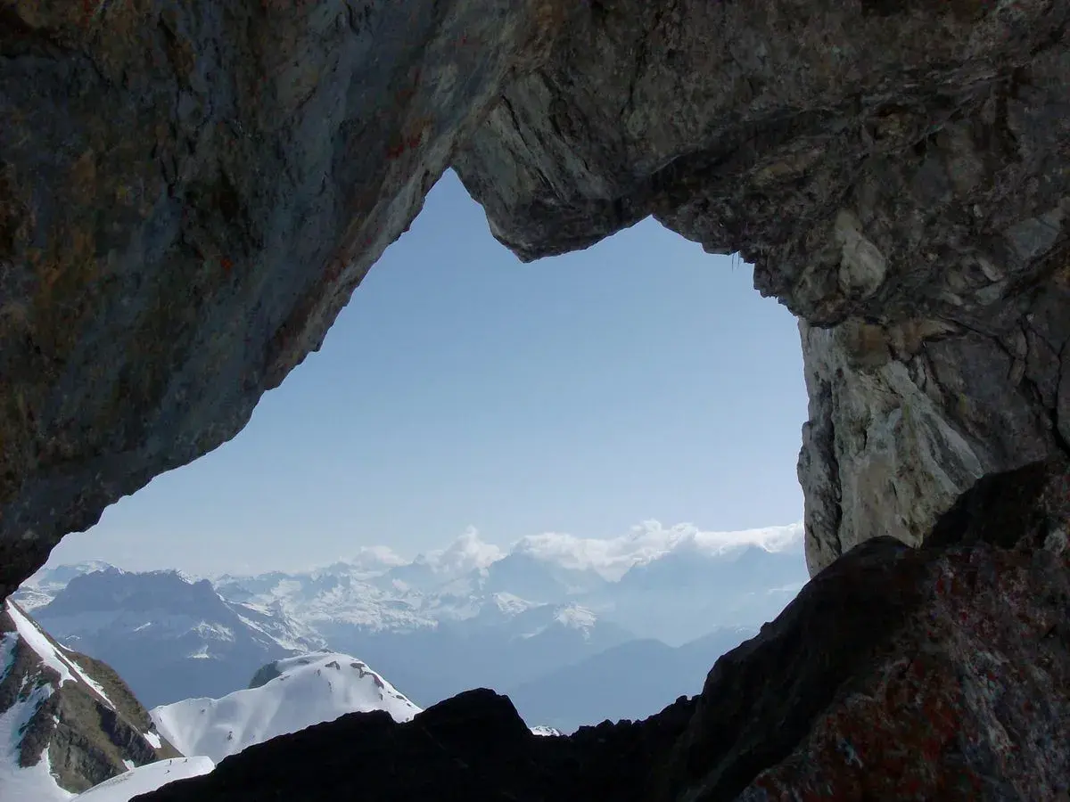 Vue spectaculaire sur les montagnes enneigées depuis le "Trou de la Mouche", un passage rocheux offrant une perspective unique lors d'une randonnée.