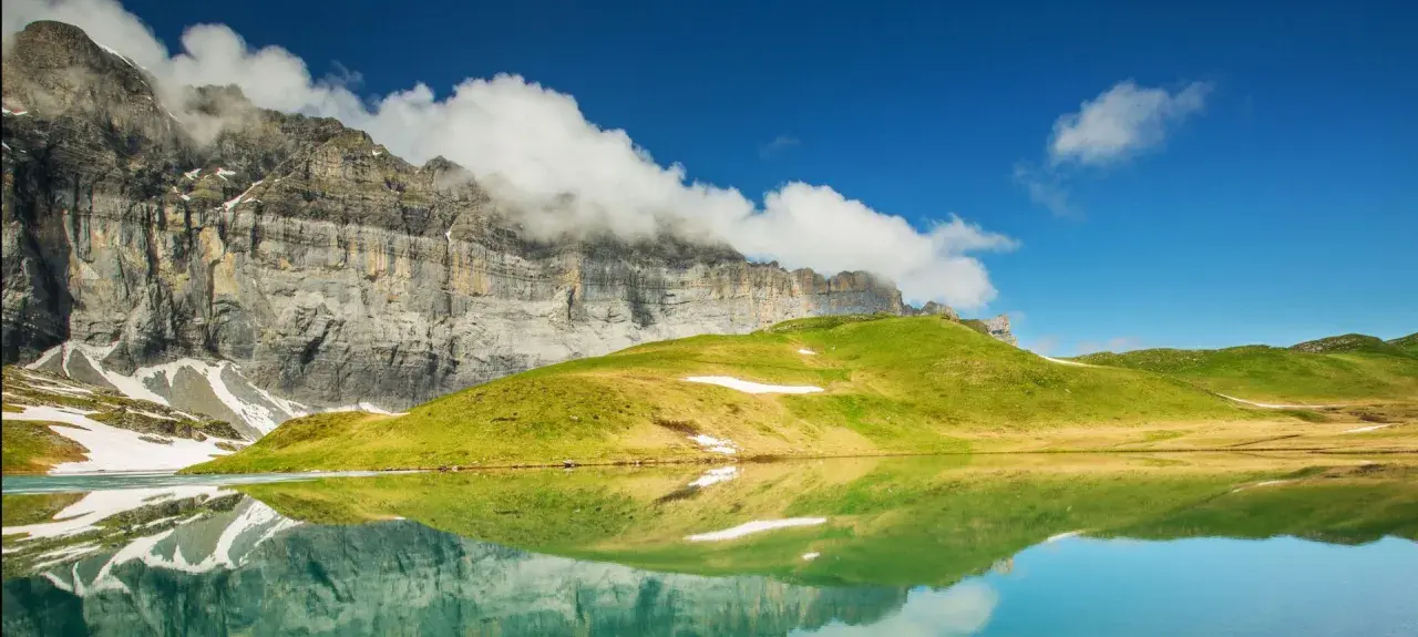 Reflets parfaits d'une montagne imposante et d'une colline verdoyante dans un lac alpin paisible, évoquant la sérénité du tour des Fiz.