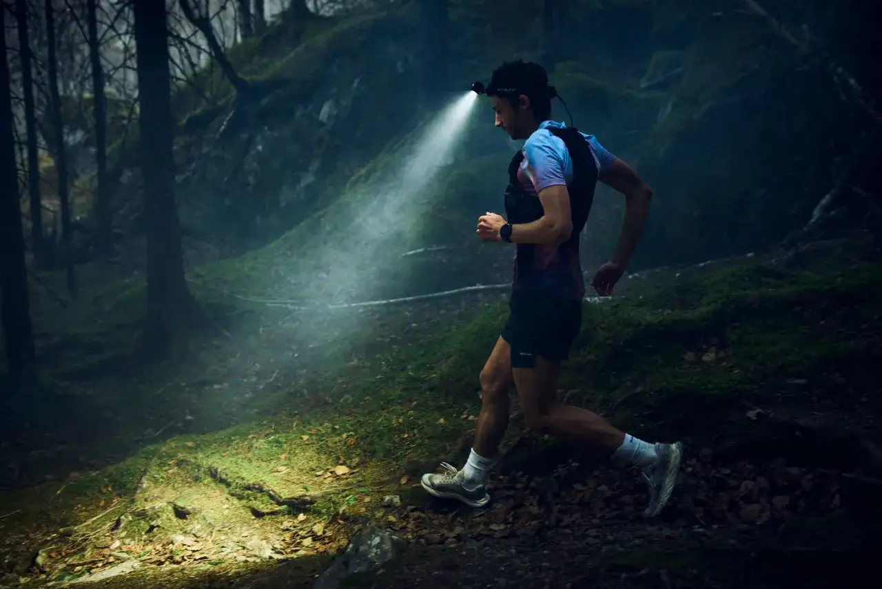 Un coureur s'aventure dans une for&ecirc;t sombre, &eacute;clair&eacute; par une lampe frontale. Une v&eacute;ritable randonn&eacute;e nocturne.