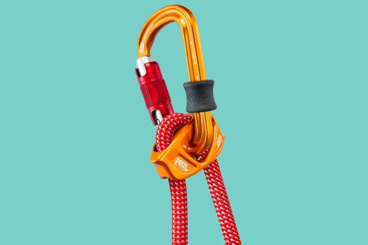 Un mousqueton Petzl orange et rouge avec une corde rouge et blanche, prêt pour une vache escalade audacieuse.