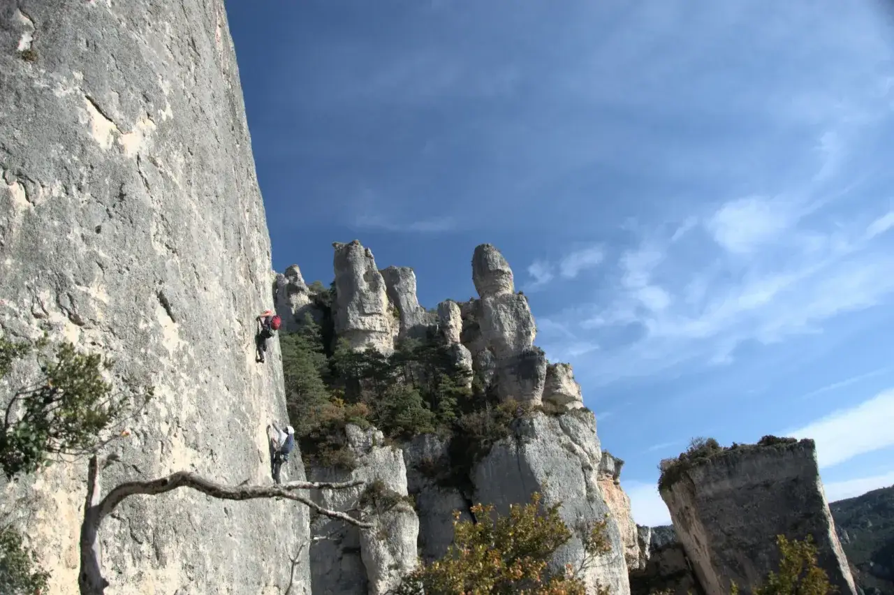 Deux grimpeurs s'&eacute;l&egrave;vent sur une paroi rocheuse abrupte, une sc&egrave;ne d'escalade extr&ecirc;me sous un ciel bleu &eacute;clatant.