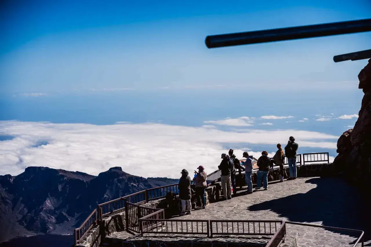 Vue depuis le pico mas alto de Espa&ntilde;a, des touristes admirent la mer de nuages sous un ciel bleu &eacute;clatant.