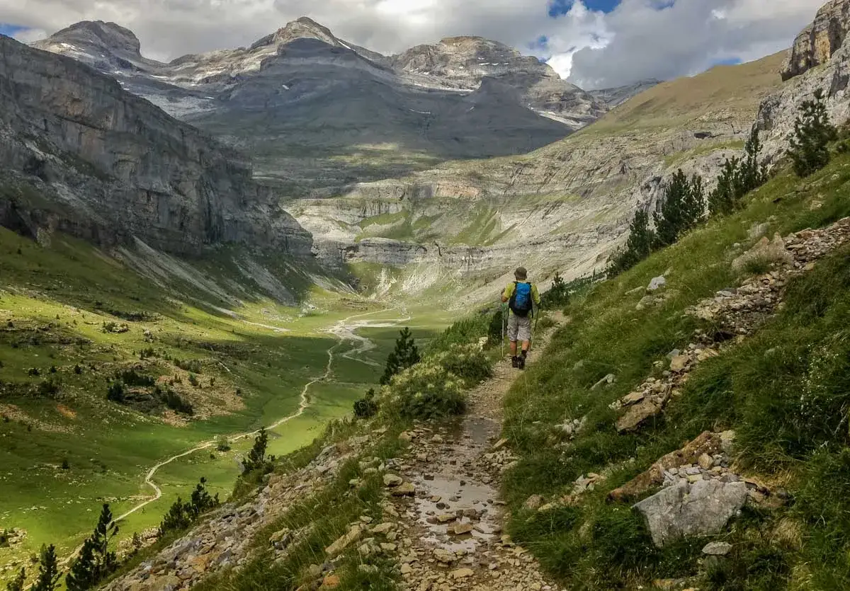 Randonneur explorant la selva de Oza, un paysage de montagne spectaculaire avec une vallée verdoyante et un sentier rocailleux.
