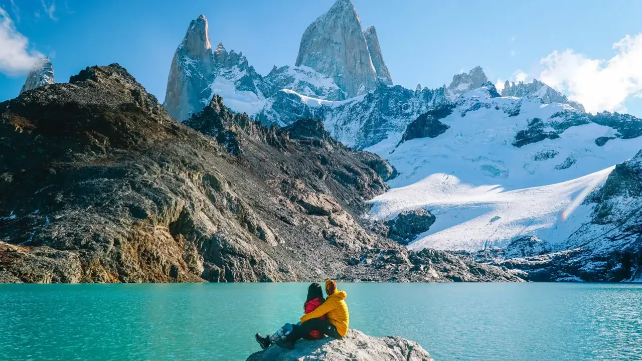 Un couple admire la majesté des montagnes de Patagonie, un lac turquoise à leurs pieds.