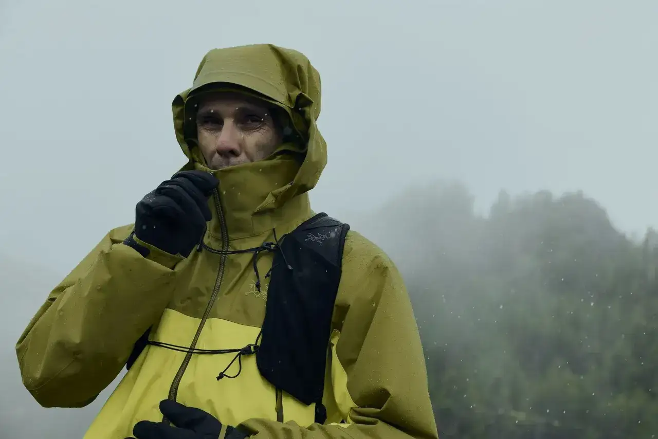 Un homme en veste jaune et verte, par temps de pluie, montre l'efficacité du Gore-Tex pour rester au sec.