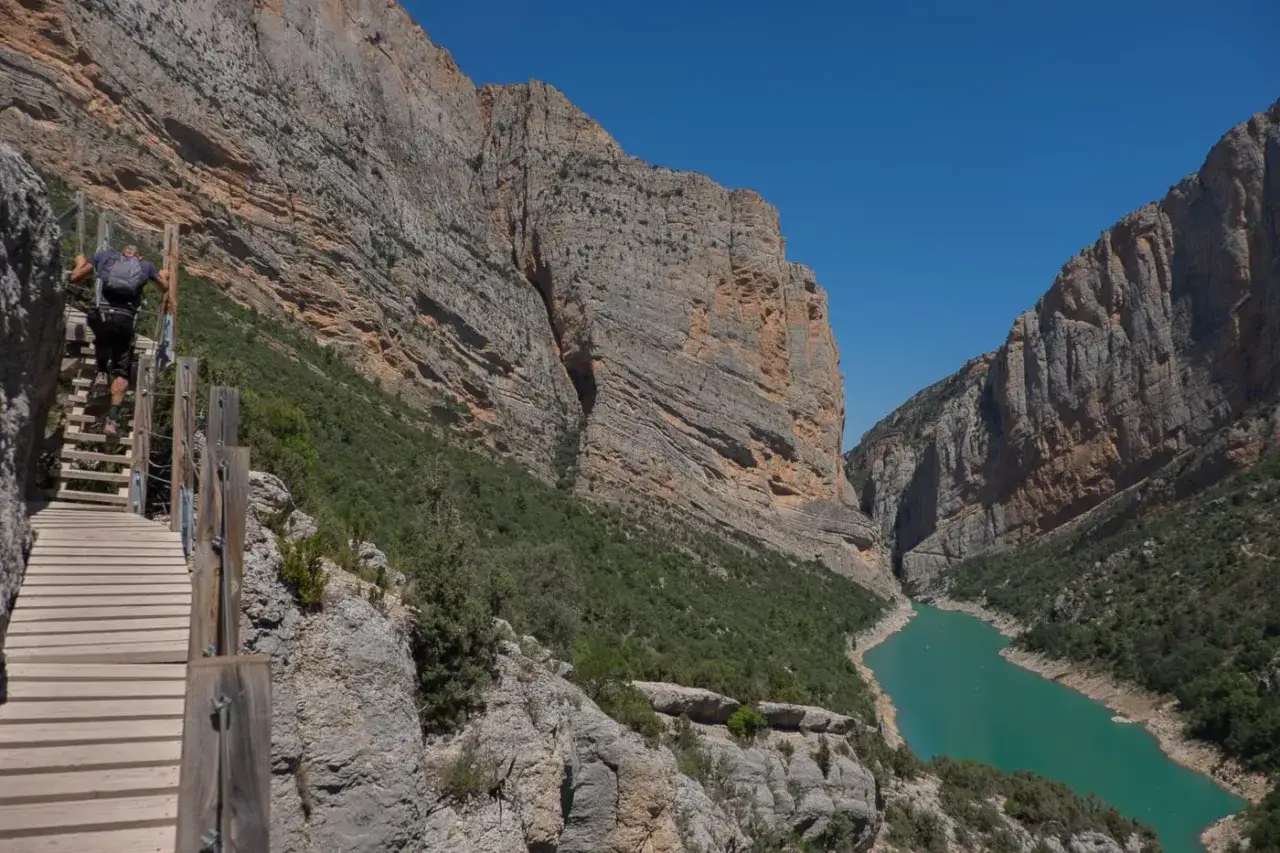 Un randonneur escalade les pasarelas de Montfalc&oacute;, un sentier vertigineux au-dessus d'un canyon aux falaises imposantes et d'une eau turquoise.