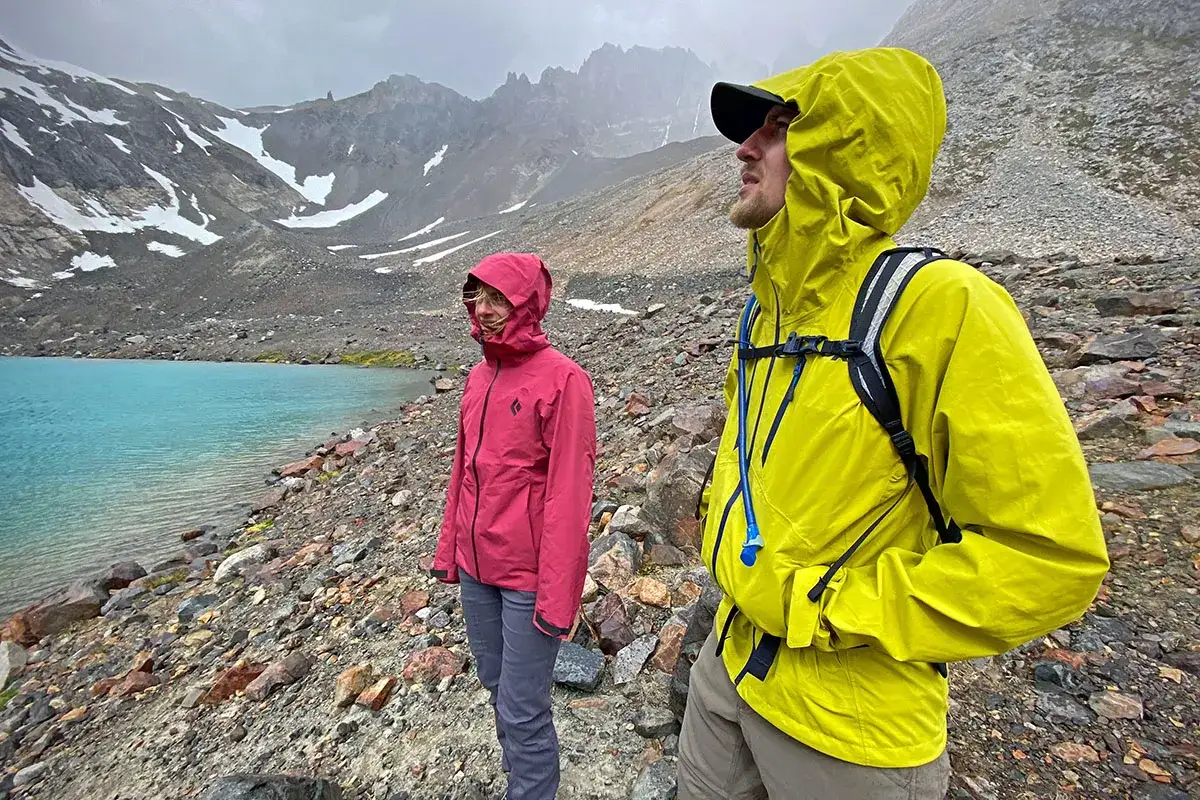 Deux randonneurs, l'un en veste rose, l'autre en jaune vif, contemplent un lac turquoise au pied de montagnes enneigées. Le débat primaloft vs gore-tex est ouvert.