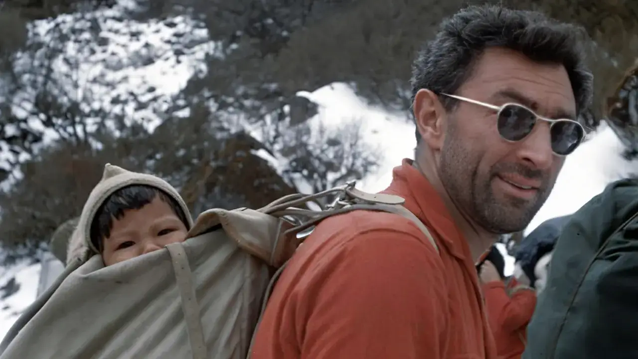 Guido Magnone, lunettes de soleil, porte un b&eacute;b&eacute; dans un sac &agrave; dos sur un sentier enneig&eacute;.