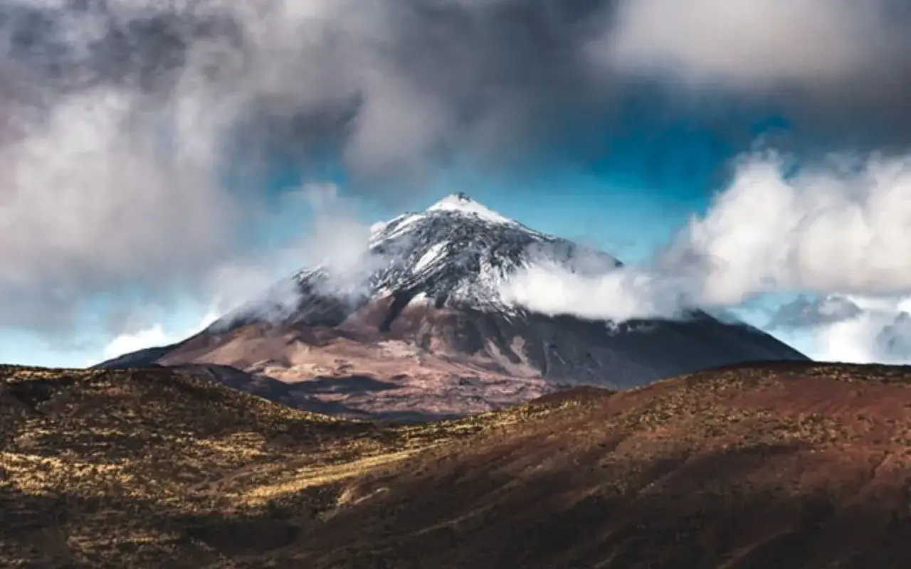 Majestueux sommet enneigé des montañas españa, émergeant des nuages cotonneux. Paysage volcanique aux teintes ocres.