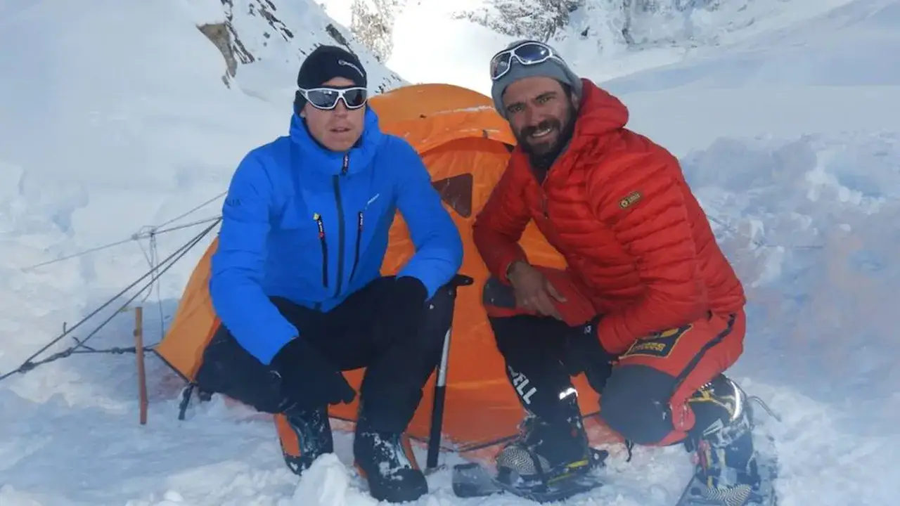 Deux alpinistes, dont Daniele Nardi, posent devant une tente orange dans un paysage enneigé.